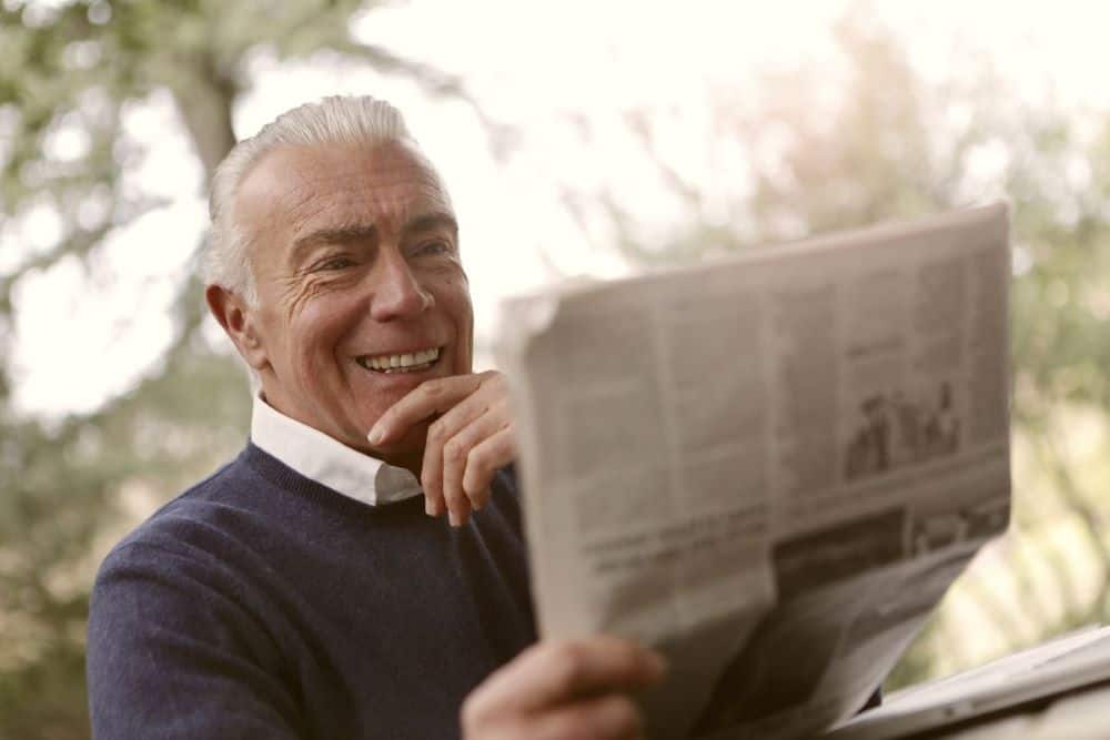 An older man with white hair reads a newspaper.
