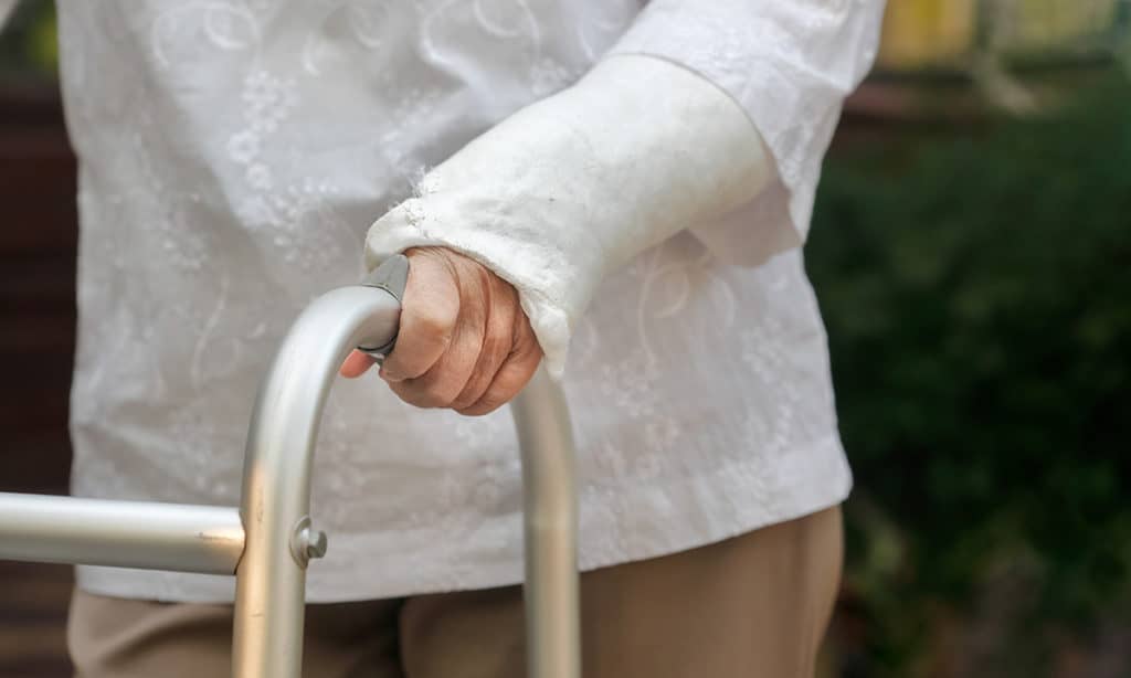 A senior woman with a walker and an injured arm in a cast